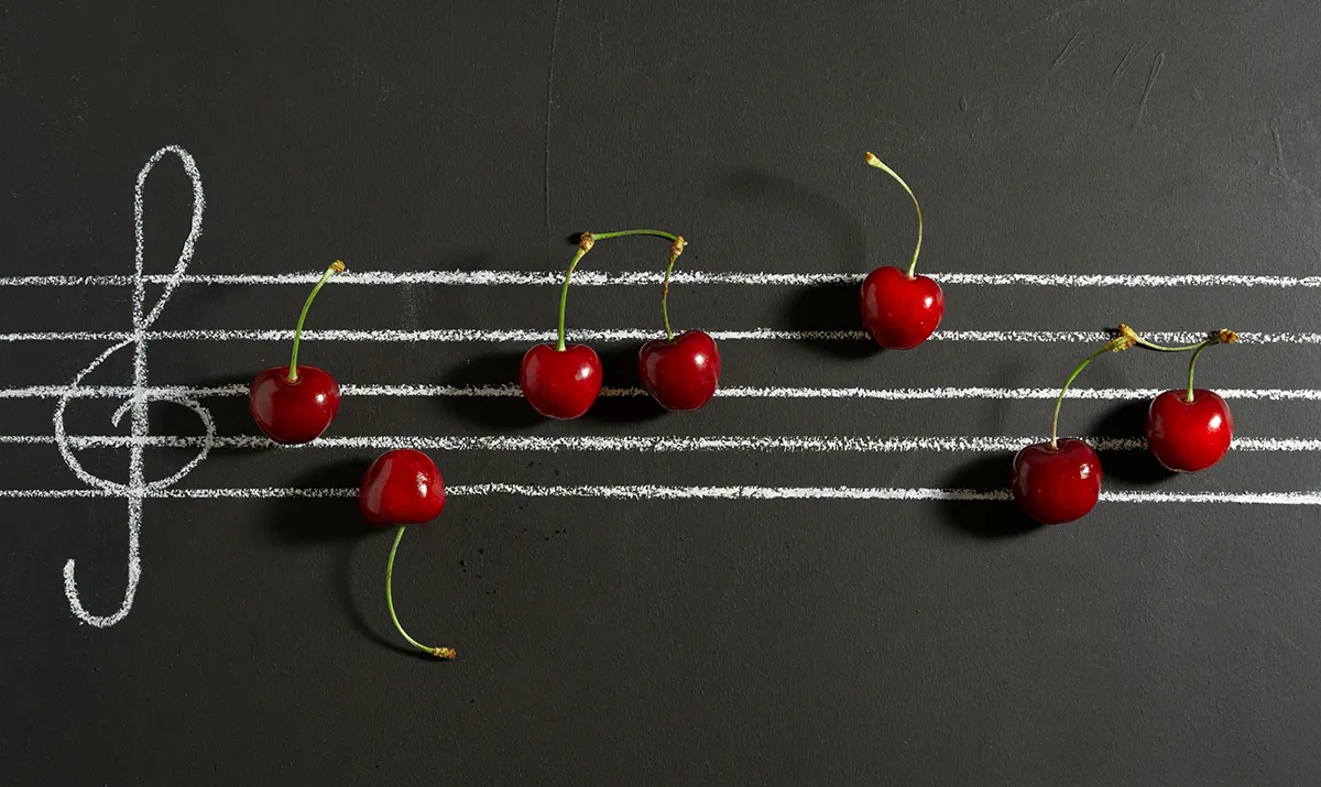 Pentagrama pintado en un pizarrón con cerezas simulando notas musicales