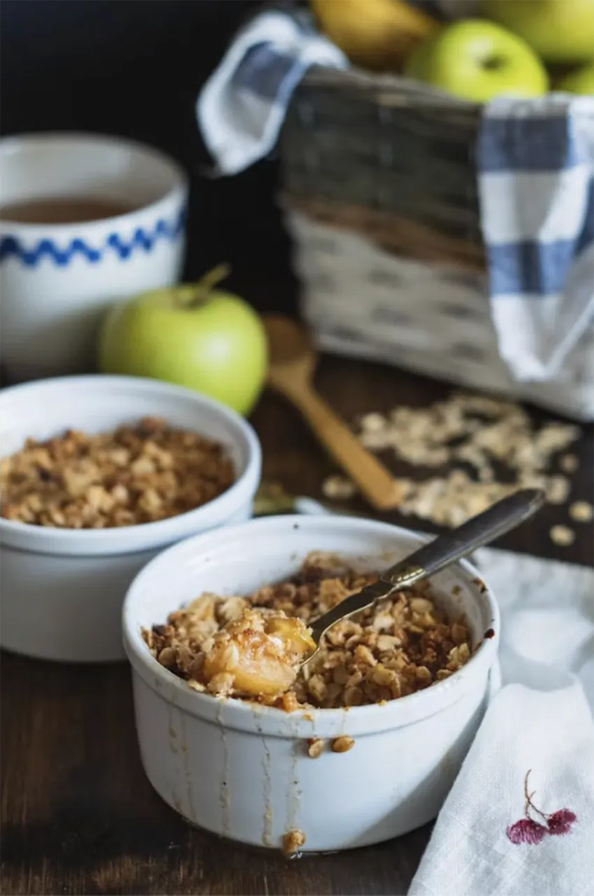 Crumble de manzana y canela con fondo de manzanas verdes dentro de una canasta