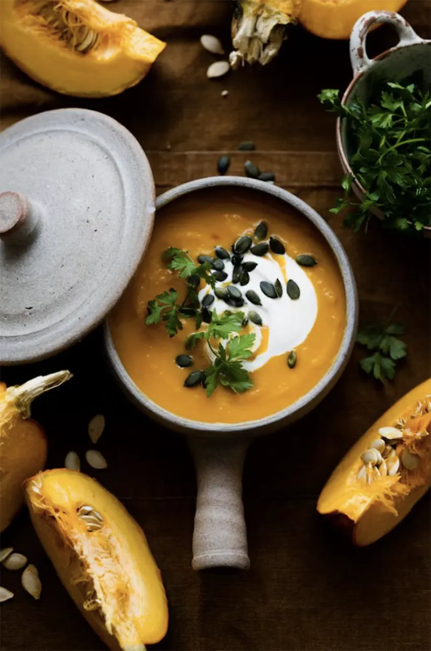 Crema de calabaza rostizada acompañada de trozos de calabaza fresca sobre una mesa de madera